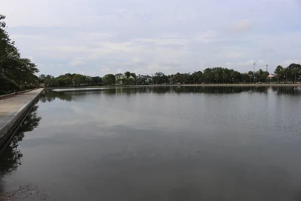 The still water of Colonial Lake reflecting the sky, with a stone edge on the left and trees along the far side
