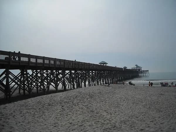 The long wooden Folly Beach fishing pier stretching out over the ocean from the sand on an overcast day