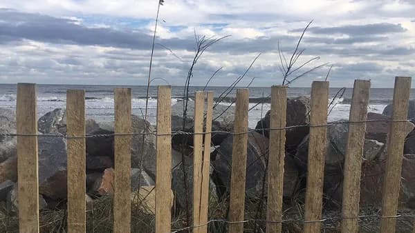 A weathered wooden picket fence in front of jetty rocks pushed ashore by Hurricane Irma at the Washout
