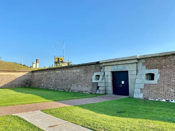 The brick wall of Fort Moultrie with its arched sally port entrance, behind a green lawn and path