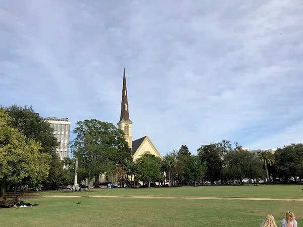 The open lawn of Marion Square with trees and a church steeple rising behind it under a cloudy sky