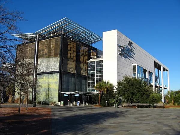The glass-fronted South Carolina Aquarium building with a steel canopy, seen from its plaza on a clear day