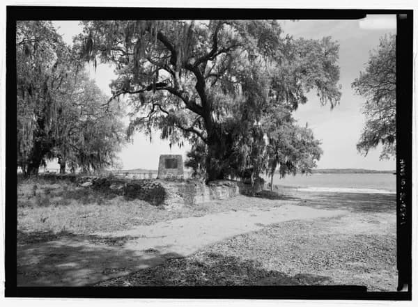 Black-and-white photograph of a large live oak over low tabby walls beside the water at Fort Frederick