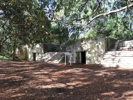 Concrete walls, doorways and stairs of the Fort Fremont battery, seen from the rear under shading trees