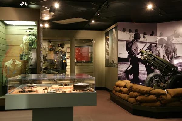 Museum exhibit hall with display cases, a uniformed mannequin and a field gun beside sandbags