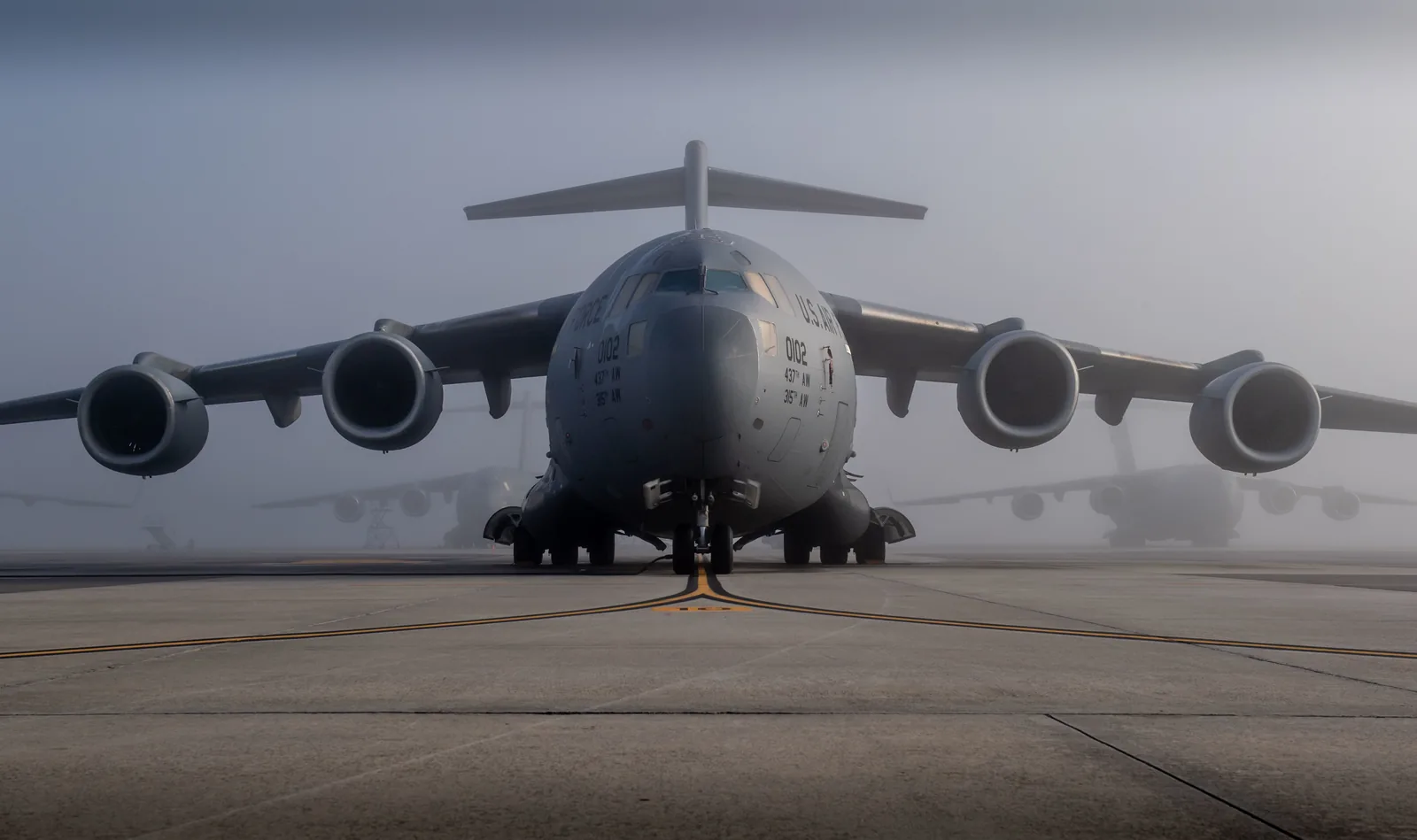 A gray C-17 Globemaster III cargo plane parked on the flightline at Joint Base Charleston on a foggy morning