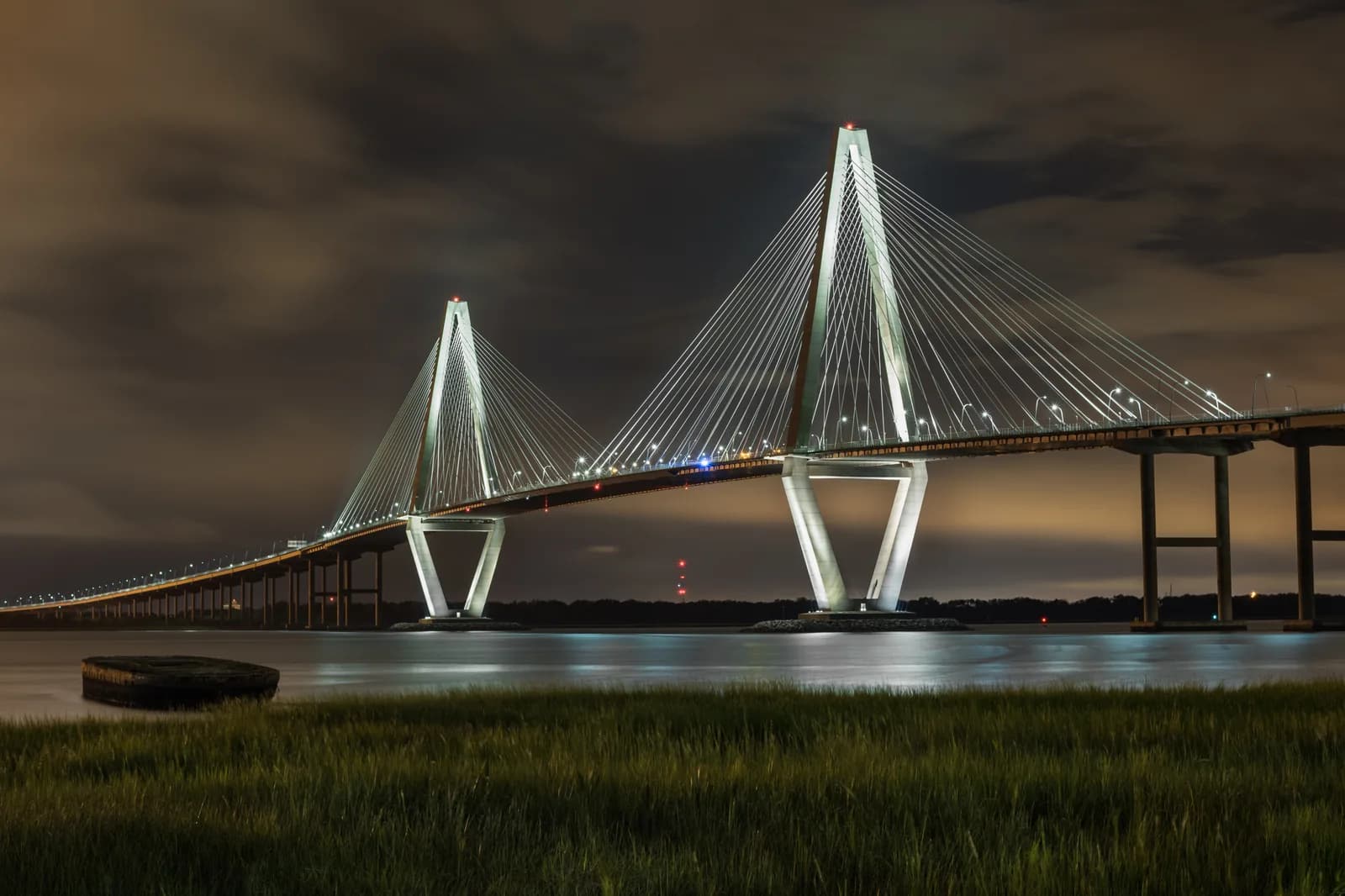The Arthur Ravenel Jr. Bridge lit up at night over the Cooper River, seen across the marsh from Mount Pleasant
