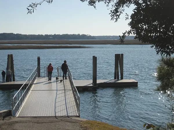 A gangway leading down to a floating public dock on the May River, with two people standing at the end