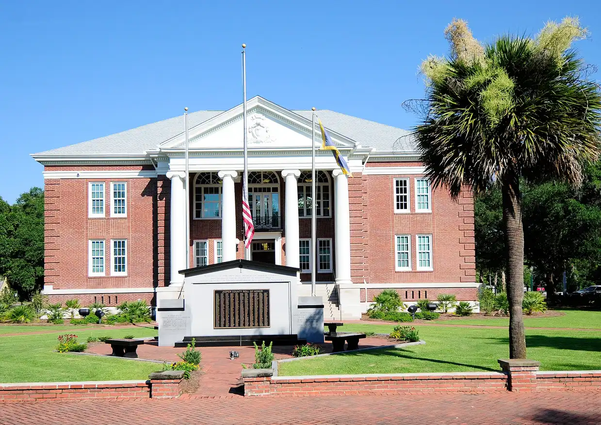 The red-brick Jasper County Courthouse with white columns and a flag, behind a lawn and a palmetto tree